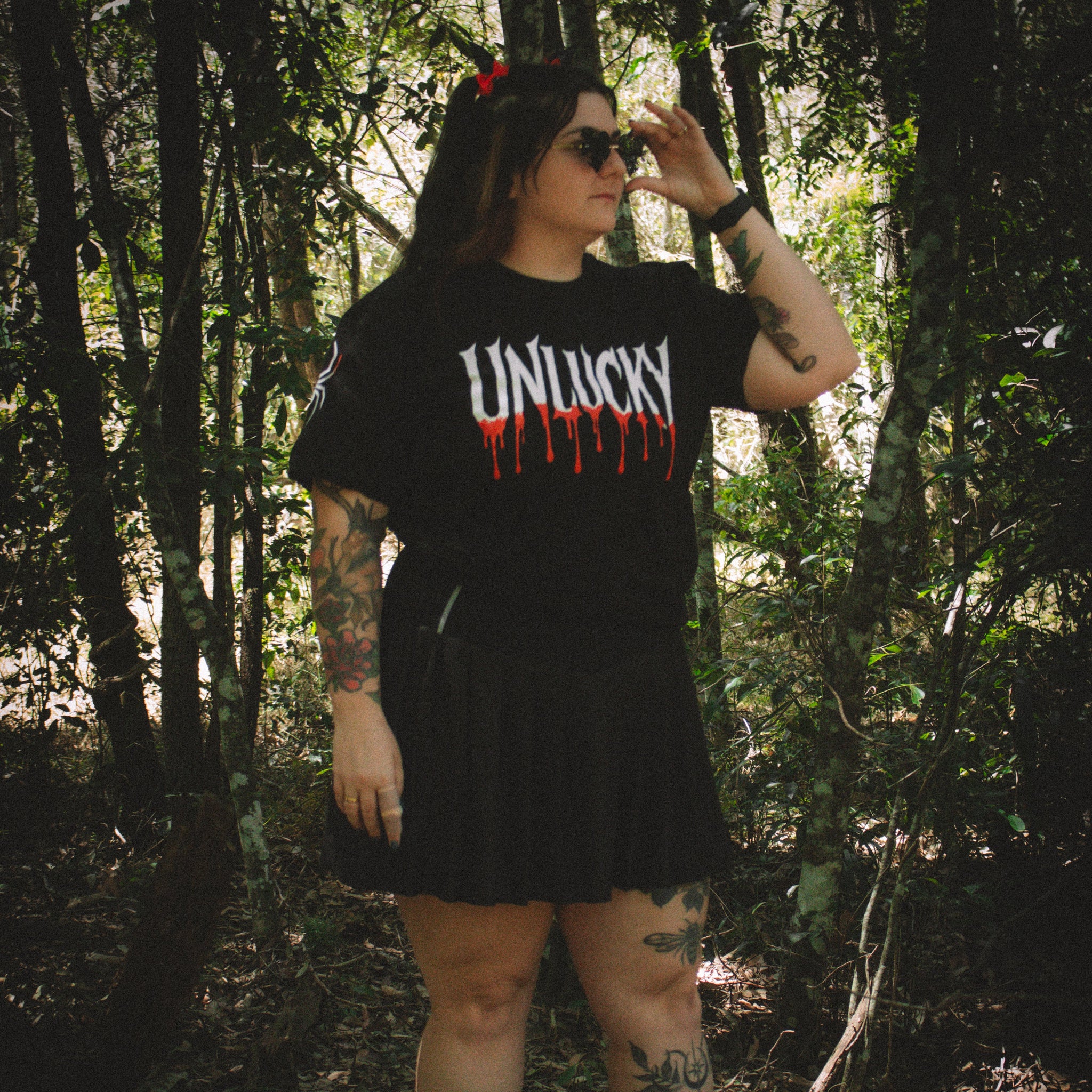 Person wearing a black t-shirt with 'UNLUCKY' printed on it in a forest setting.