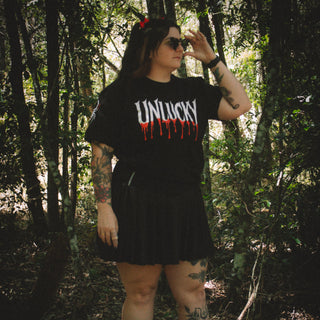 Person wearing a black t-shirt with 'UNLUCKY' printed on it in a forest setting.