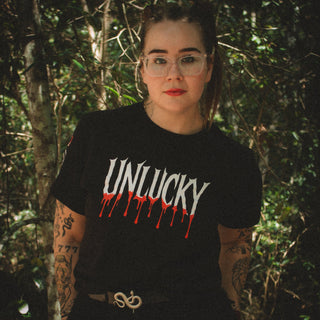 Person wearing a black t-shirt with 'UNLUCKY' text in a forest setting