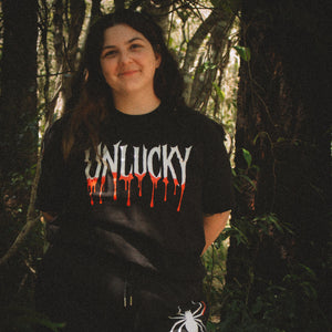 Person wearing a black t-shirt with 'UNLUCKY' design in a forest setting