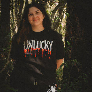 Person wearing a black t-shirt with 'UNLUCKY' design in a forest setting