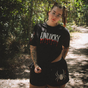 Person wearing a black t-shirt with 'UNLUCKY' design in a forest setting