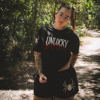 Person wearing a black t-shirt with 'UNLUCKY' design in a forest setting