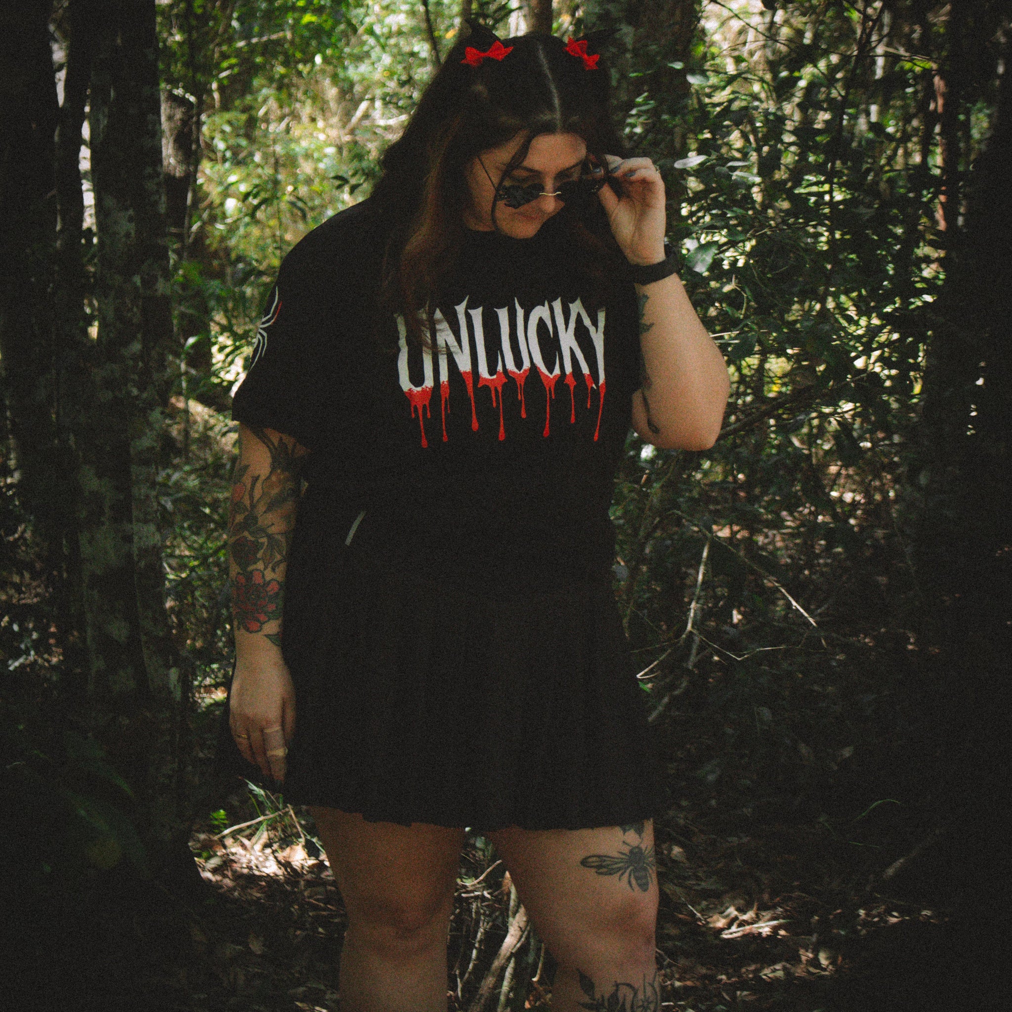 Person wearing a black t-shirt with 'UNLUCKY' printed on it in a forest setting