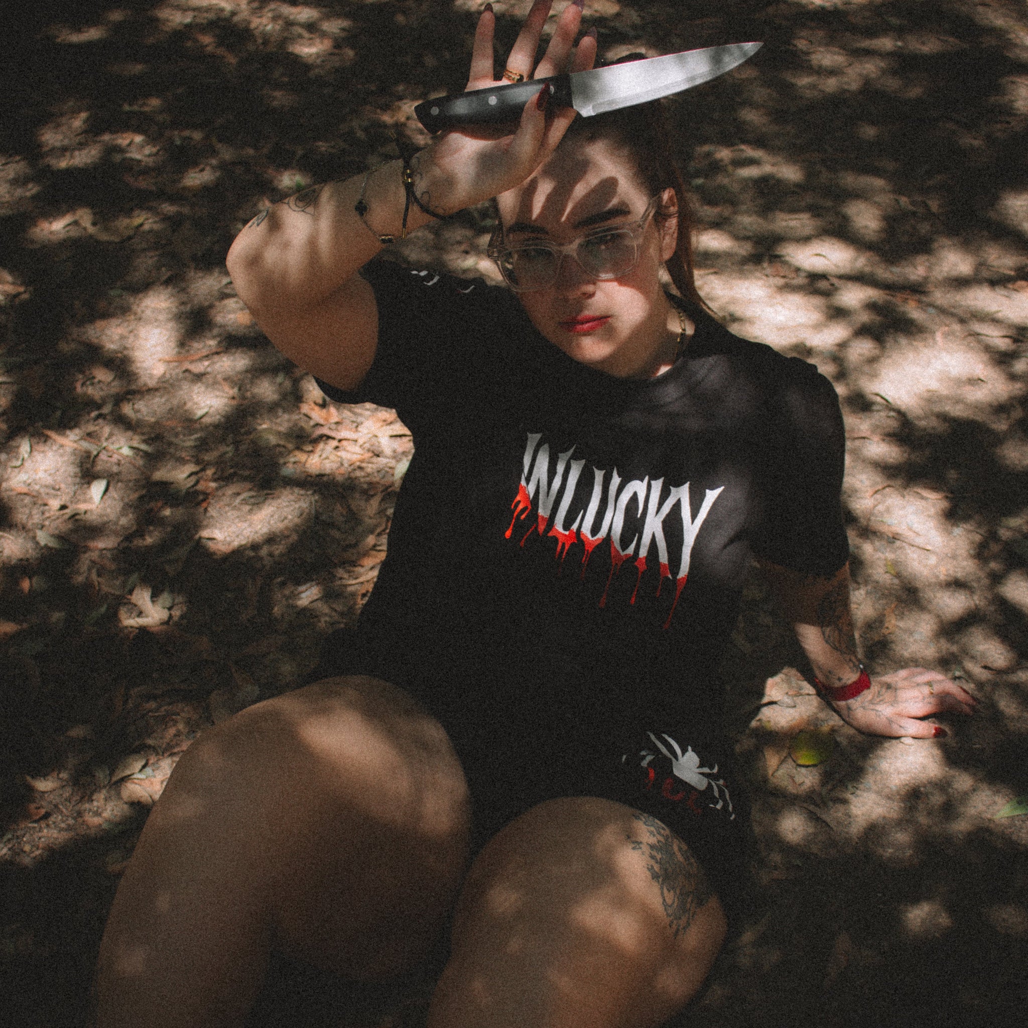Person wearing a black t-shirt with 'WILUCKY' printed on it, sitting in a forest.