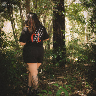 Person standing in a forest wearing a black t-shirt with red design and black shorts.
