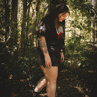 Person walking through a forest wearing a black shirt with a logo and text.