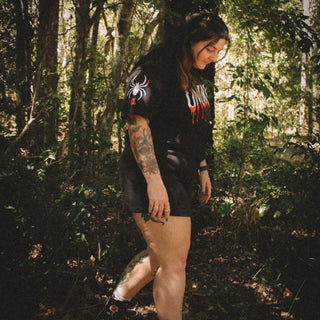 Person walking through a forest wearing a black hoodie with a logo and text.
