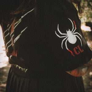 Person wearing a black hoodie with a spider logo and 'CL' letters, standing outdoors.